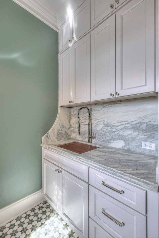 interior space featuring decorative backsplash, white cabinets, light stone counters, crown molding, and a sink