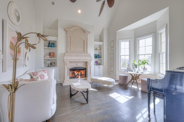 living room with a warm lit fireplace, ceiling fan, dark wood-style flooring, and built in features