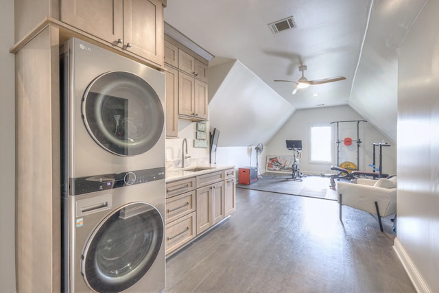 laundry room with stacked washer and clothes dryer, visible vents, dark wood-type flooring, a sink, and ceiling fan