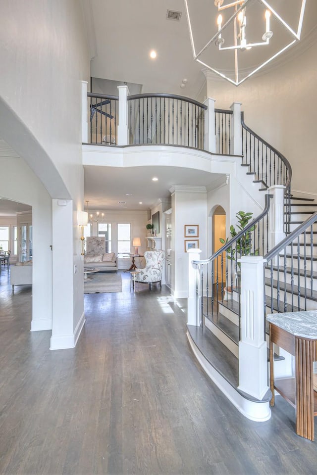 foyer entrance featuring dark wood-style floors, arched walkways, visible vents, a towering ceiling, and stairs