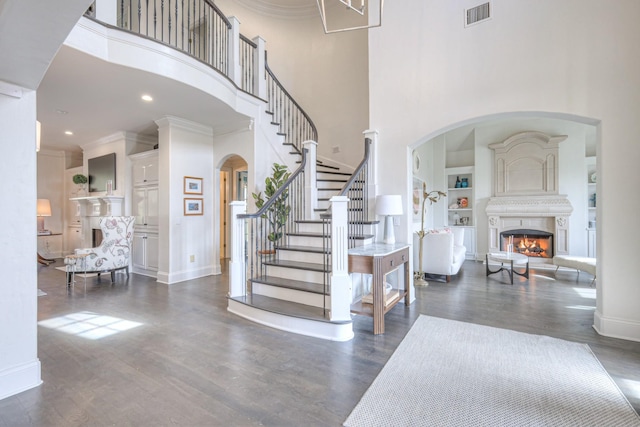 foyer with a warm lit fireplace, ornamental molding, dark wood-style flooring, and visible vents