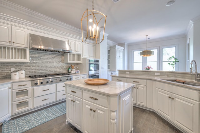 kitchen featuring white cabinets, wall chimney exhaust hood, a kitchen island, appliances with stainless steel finishes, and a sink