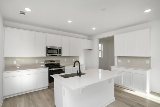 kitchen featuring a sink, white cabinets, light countertops, appliances with stainless steel finishes, and a center island with sink