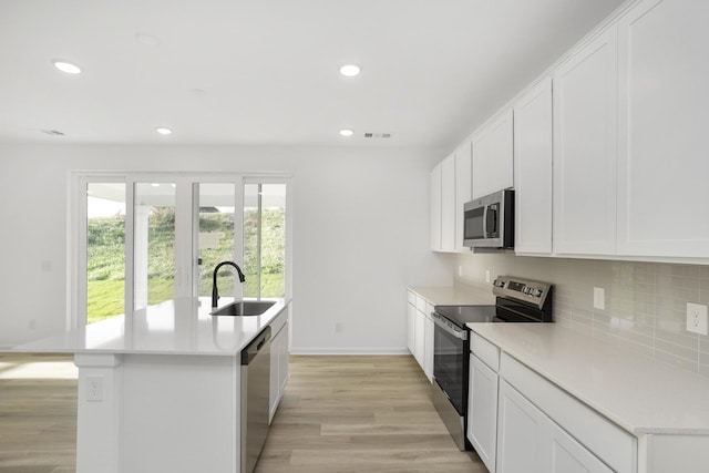 kitchen with a kitchen island with sink, stainless steel appliances, a sink, and light countertops