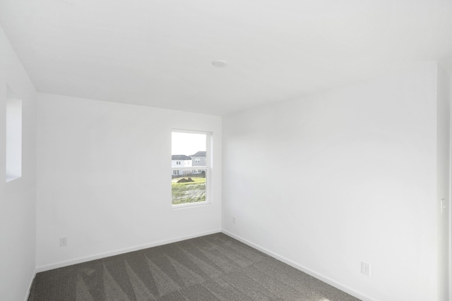 unfurnished room featuring dark carpet and baseboards