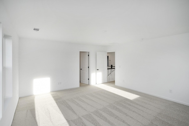 spare room with light colored carpet, visible vents, and baseboards