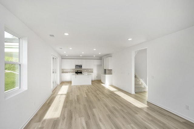 unfurnished living room featuring light wood-style flooring, recessed lighting, visible vents, baseboards, and stairway