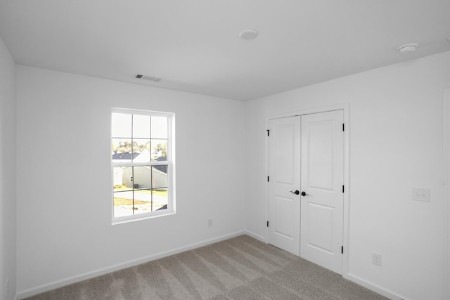 unfurnished bedroom with light carpet, baseboards, visible vents, and a closet