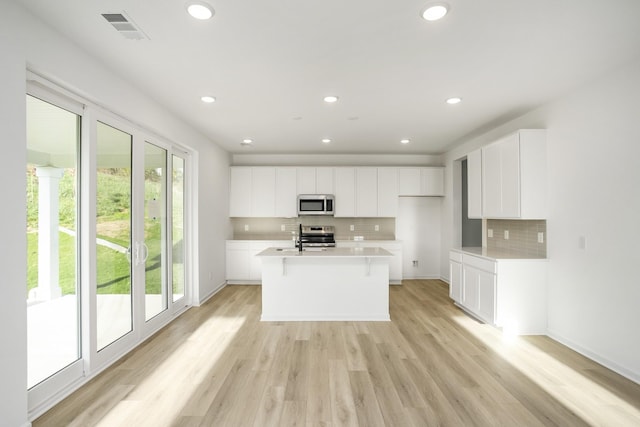 kitchen with stainless steel appliances, visible vents, white cabinetry, light countertops, and an island with sink