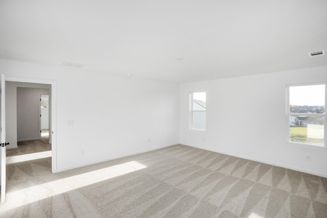 spare room with baseboards, visible vents, and light colored carpet