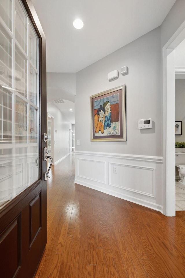 hall featuring a wainscoted wall, a decorative wall, and wood finished floors