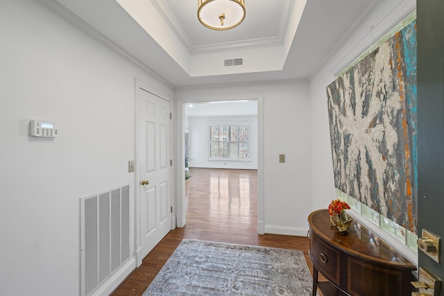 hallway featuring visible vents, baseboards, ornamental molding, a raised ceiling, and dark wood finished floors