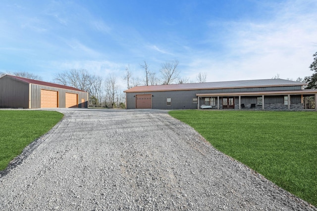 ranch-style home featuring a front yard, gravel driveway, a detached garage, and an outdoor structure