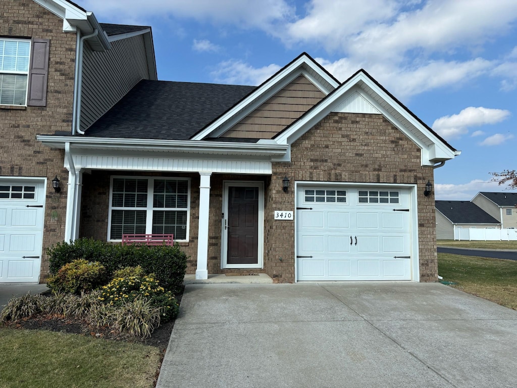 view of front of home with driveway, an attached garage, a shingled roof, and brick siding