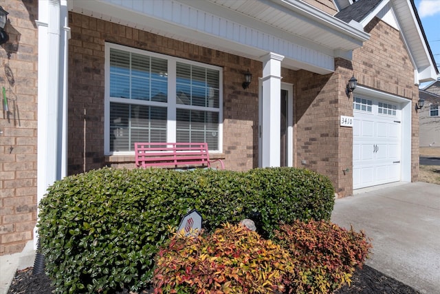 entrance to property featuring driveway, brick siding, and an attached garage