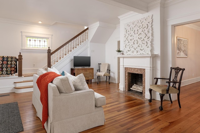 living room featuring a fireplace with flush hearth, wood finished floors, crown molding, and stairs