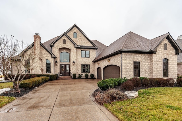 french country style house with brick siding, a chimney, a shingled roof, concrete driveway, and an attached garage