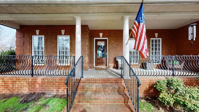 view of exterior entry with a porch and brick siding