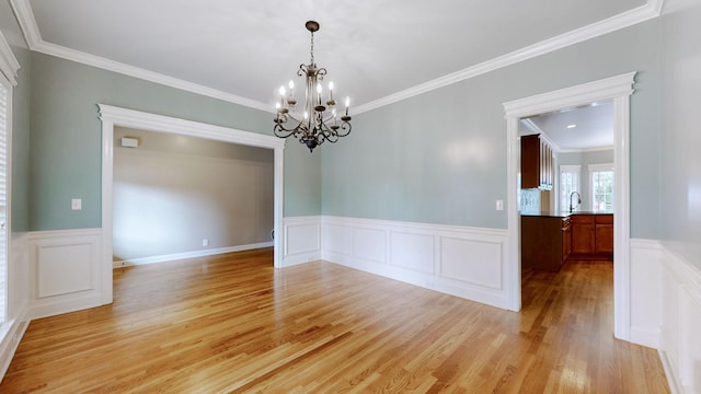 empty room featuring light wood-style flooring, a notable chandelier, a sink, ornamental molding, and wainscoting