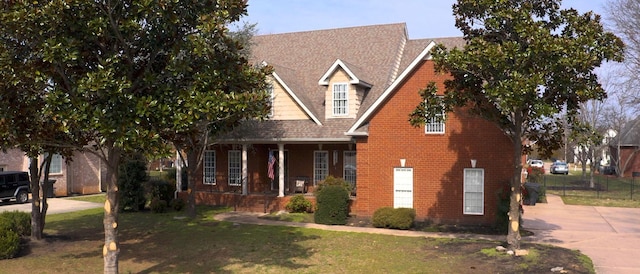 view of front facade with covered porch, brick siding, fence, concrete driveway, and a front yard