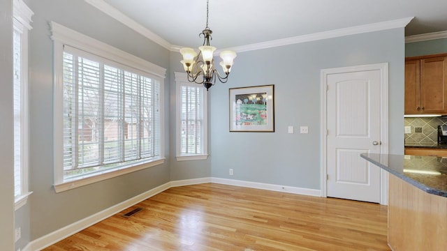 unfurnished dining area with baseboards, light wood finished floors, an inviting chandelier, and crown molding