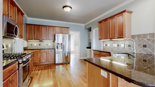 kitchen with brown cabinetry, dark stone countertops, a peninsula, stainless steel appliances, and a sink