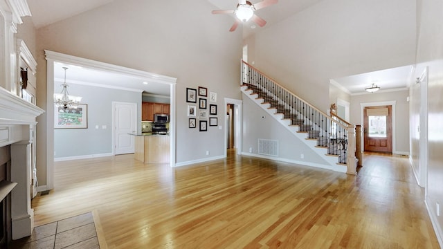 unfurnished living room featuring a fireplace, visible vents, light wood-style flooring, a high ceiling, and stairs