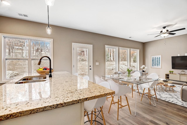 kitchen featuring visible vents, light stone counters, wood finished floors, pendant lighting, and a sink