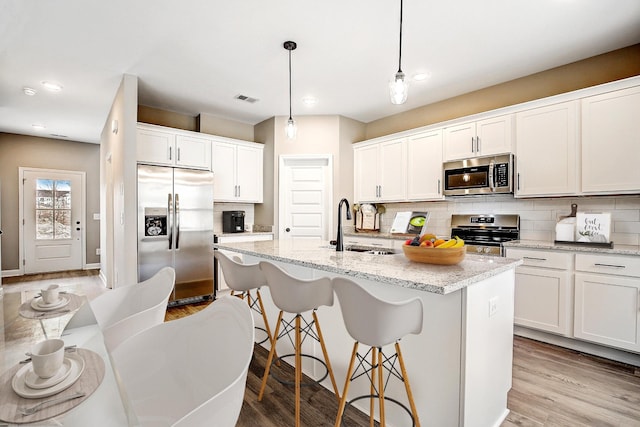 kitchen with decorative light fixtures, appliances with stainless steel finishes, a kitchen island with sink, white cabinets, and a sink