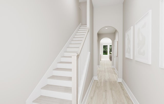 staircase featuring arched walkways, a high ceiling, baseboards, and wood finished floors