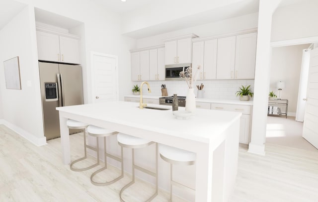 kitchen with light countertops, appliances with stainless steel finishes, an island with sink, and white cabinets