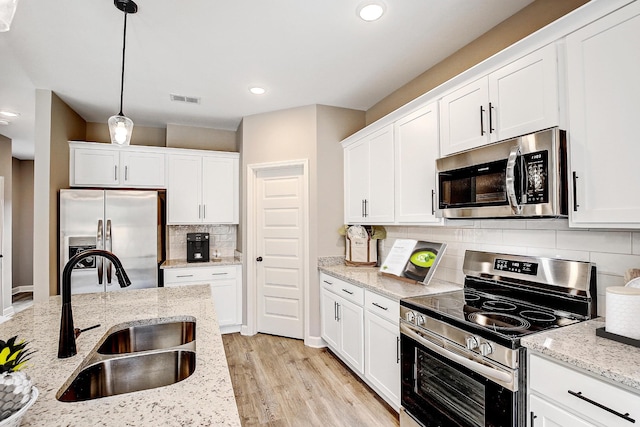 kitchen featuring hanging light fixtures, appliances with stainless steel finishes, a sink, and light stone counters