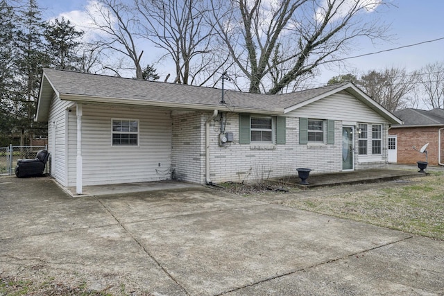 view of front of home featuring concrete driveway, brick siding, roof with shingles, and fence