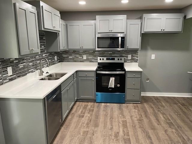 kitchen with stainless steel appliances, light countertops, a sink, and gray cabinetry