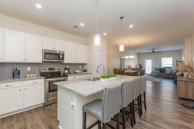 kitchen with appliances with stainless steel finishes, open floor plan, white cabinets, a sink, and an island with sink