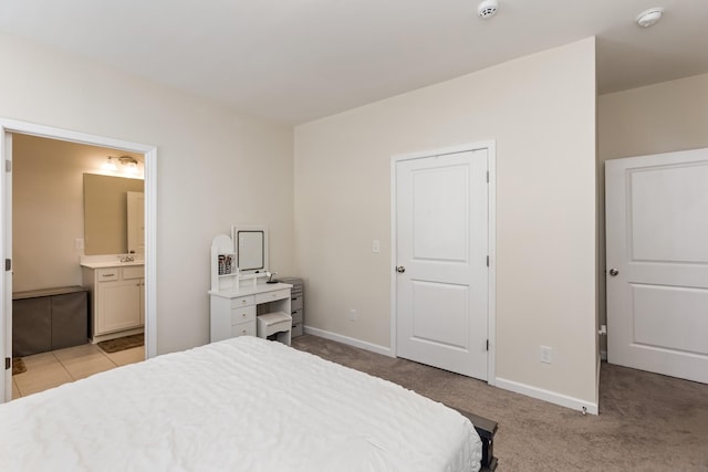 bedroom featuring ensuite bathroom, a sink, light colored carpet, and baseboards