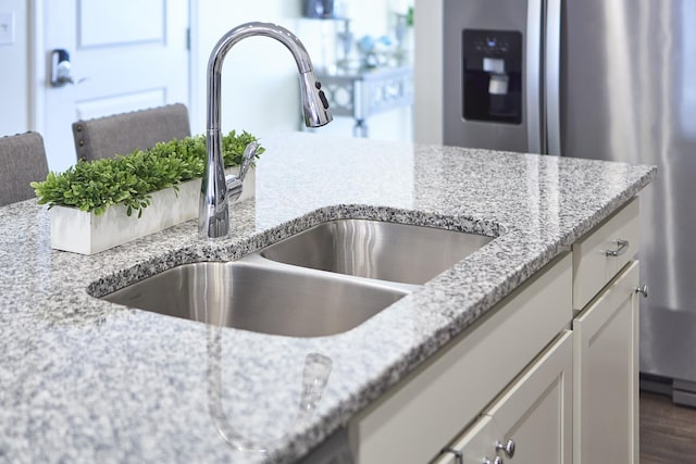 room details featuring white cabinets, a sink, stainless steel fridge with ice dispenser, and light stone countertops