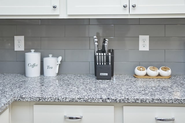 room details with white cabinets, decorative backsplash, and light stone countertops