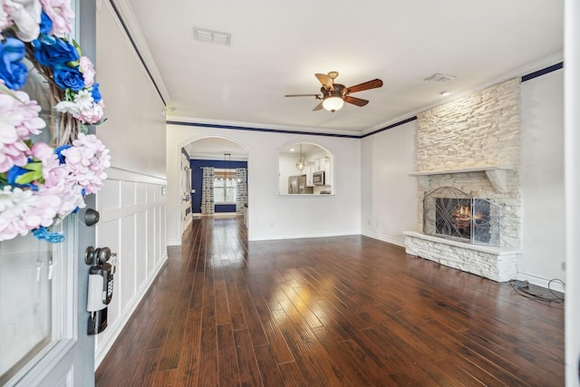 unfurnished living room featuring visible vents, arched walkways, ornamental molding, and a stone fireplace