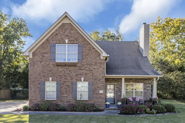 traditional-style home with a shingled roof, a chimney, a front lawn, and brick siding