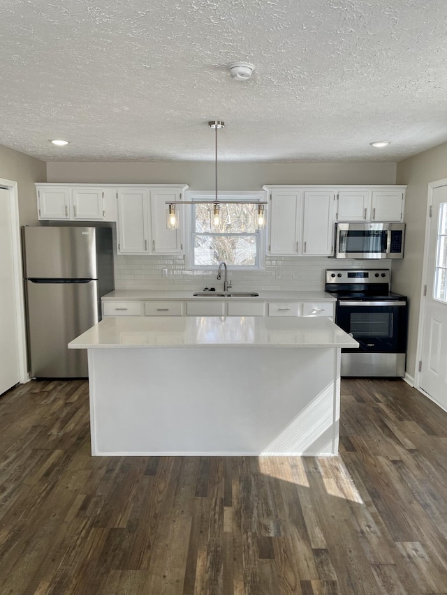 kitchen with stainless steel appliances, pendant lighting, light countertops, and white cabinets