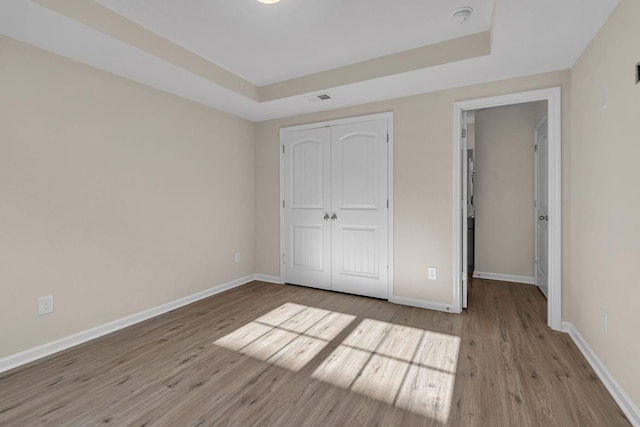 unfurnished bedroom featuring light wood-style floors, a raised ceiling, a closet, and baseboards