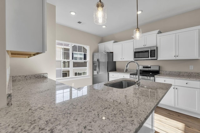 kitchen with pendant lighting, stainless steel appliances, visible vents, white cabinetry, and a sink