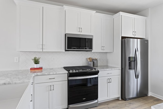 kitchen with light stone counters, light wood-style flooring, stainless steel appliances, white cabinets, and decorative backsplash