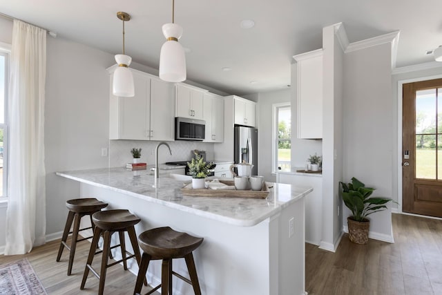 kitchen featuring hanging light fixtures, appliances with stainless steel finishes, white cabinetry, a peninsula, and a kitchen bar