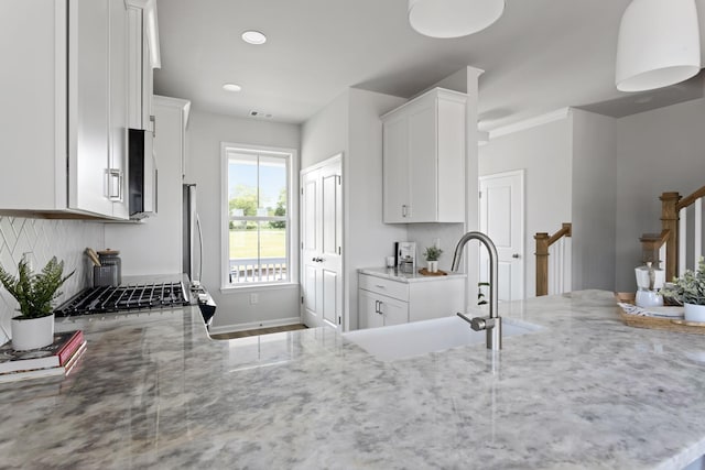 kitchen featuring white cabinets, a sink, backsplash, and light stone countertops