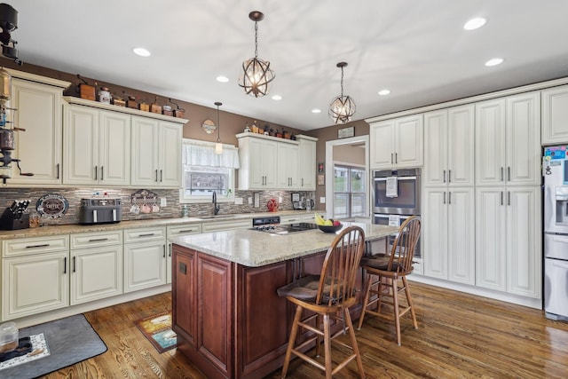 kitchen with a breakfast bar area, light stone counters, decorative light fixtures, a center island, and a sink