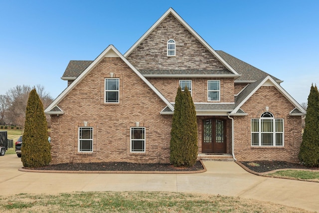 view of front facade with french doors, brick siding, and roof with shingles