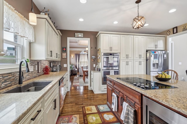 kitchen with stainless steel appliances, hanging light fixtures, a sink, and light stone countertops