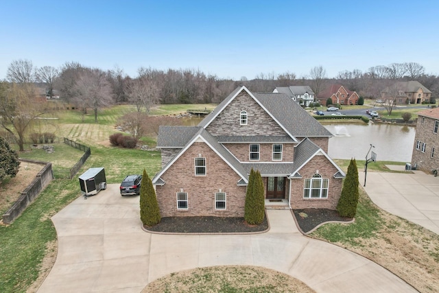 traditional home featuring a water view, roof with shingles, concrete driveway, and brick siding